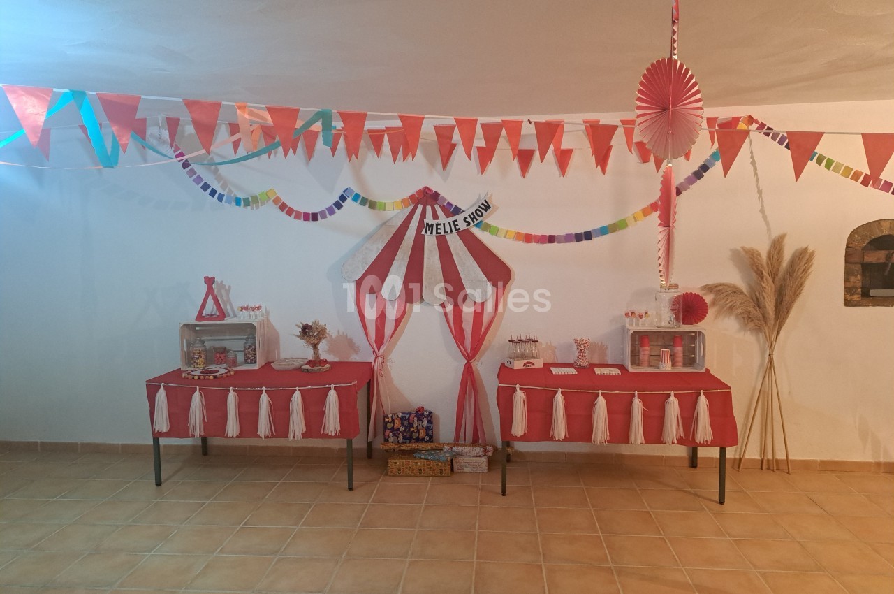 Décoration festive sur le thème du cirque avec guirlandes, tables rouges et blanches, et accessoires colorés.