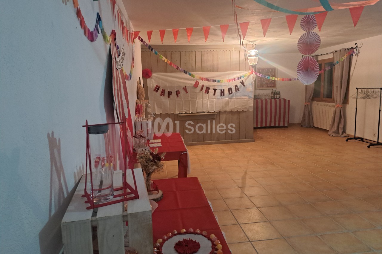 Salle décorée pour un anniversaire avec guirlandes colorées, table dressée et bannière ’Happy Birthday’.