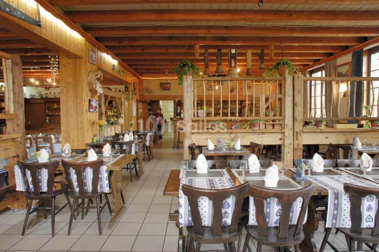 Salle de restaurant rustique avec tables en bois dressées, nappes à motifs et décoration chaleureuse en bois.