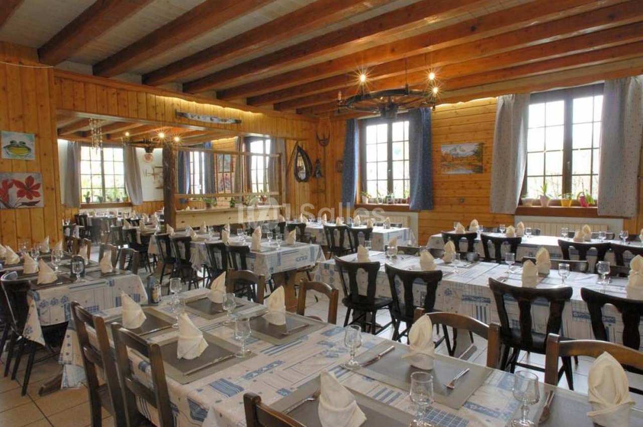 Salle de restaurant lumineuse avec tables dressées, nappes à motifs bleus et poutres apparentes au plafond.