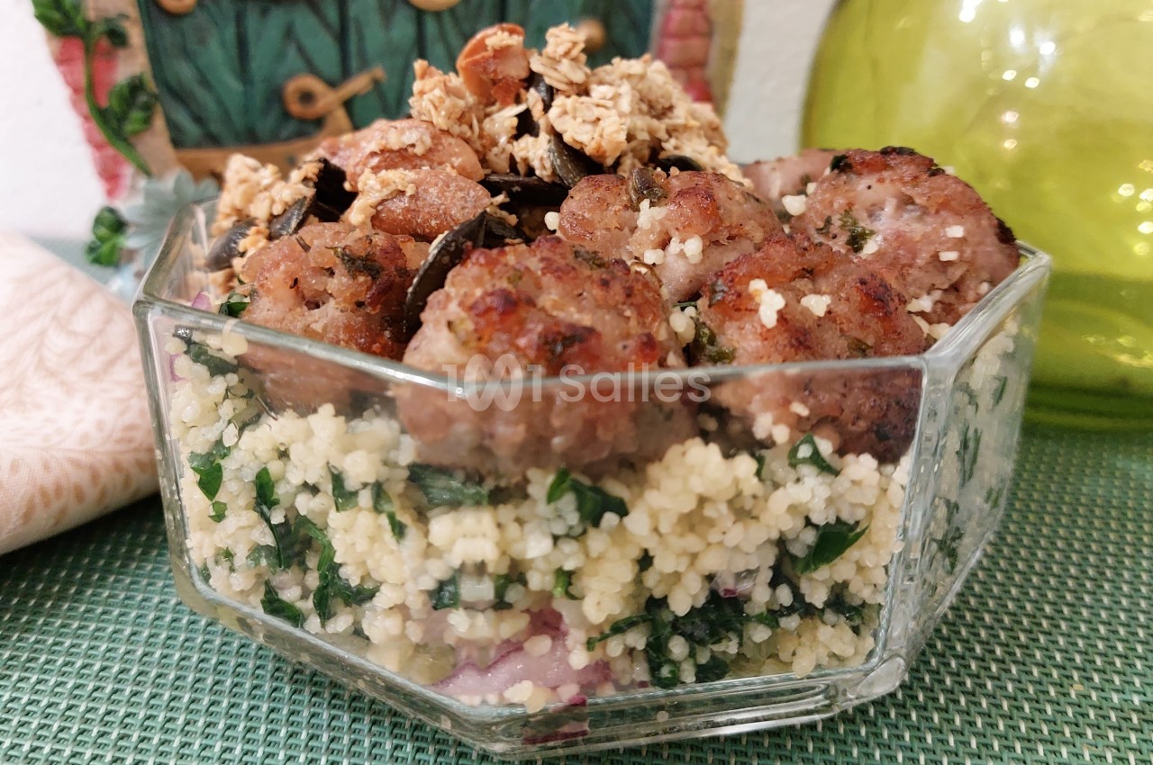Boulettes de viande grillées servies sur un lit de couscous aux herbes, garnies de céréales croustillantes.