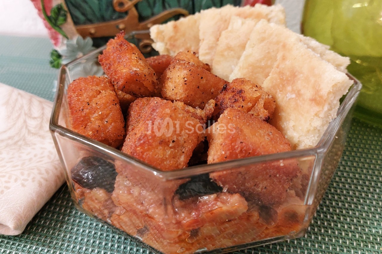 Cubes de pain dorés accompagnés de morceaux de pain plat dans un bol en verre, posés sur une nappe verte.