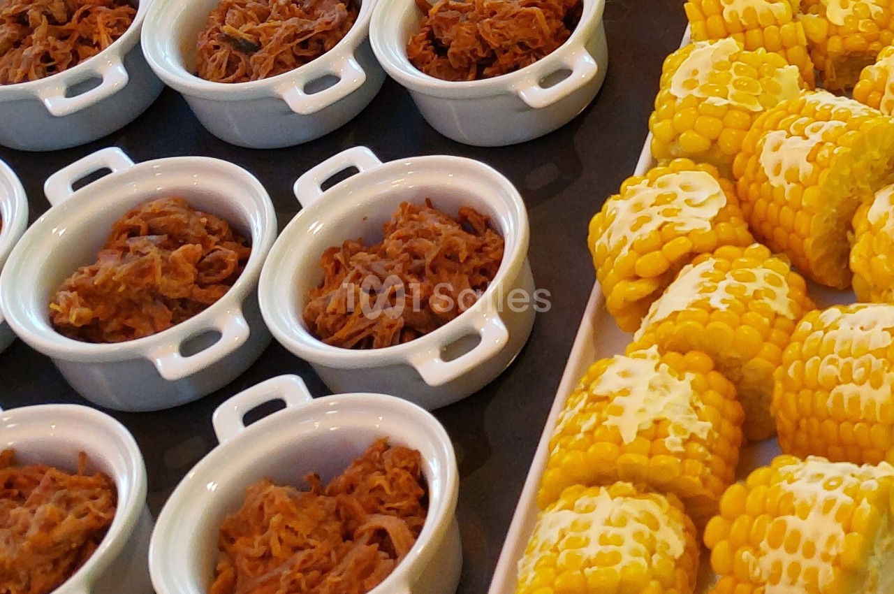 Petits plats de viande effilochée et épis de maïs coupés en morceaux disposés sur une table.