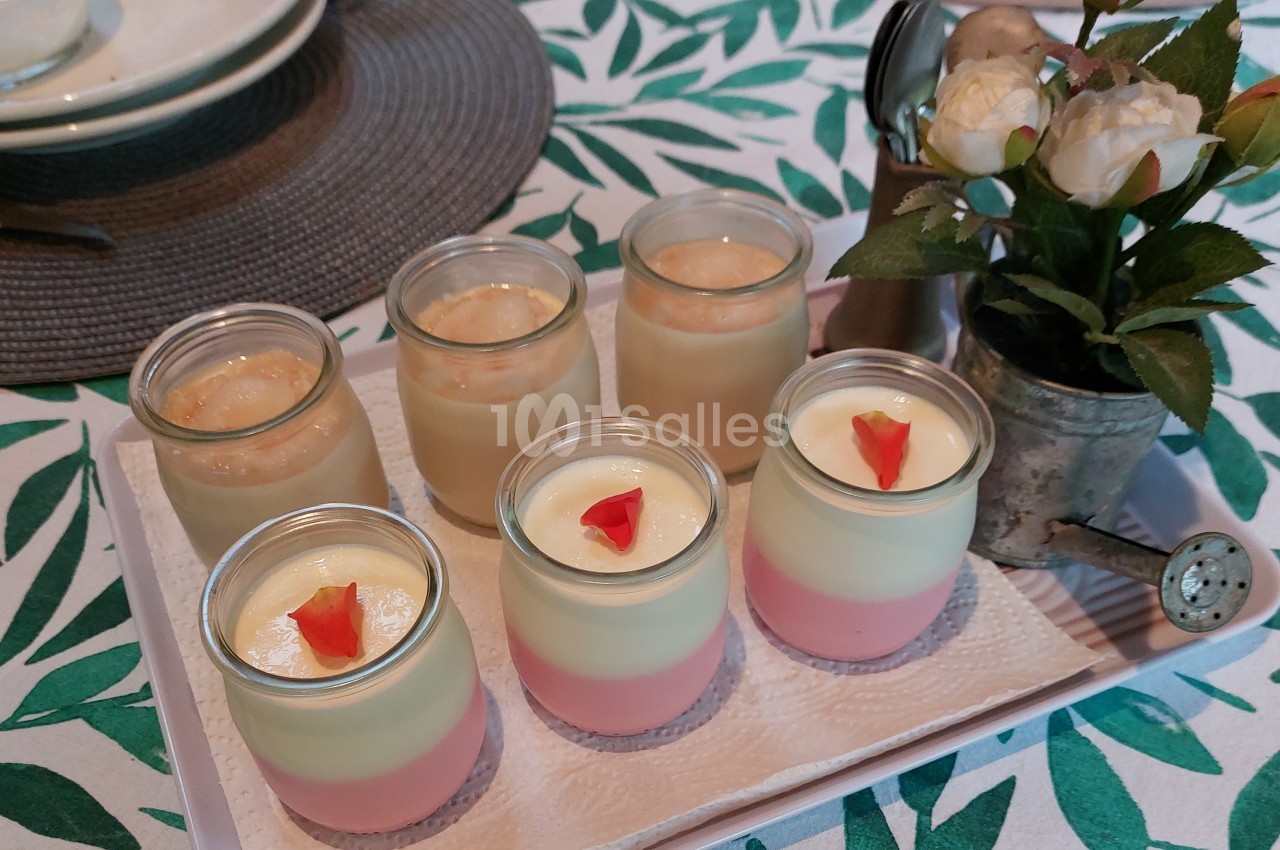 Desserts en verrines colorées sur un plateau, accompagnés d'une petite décoration florale sur une nappe à motifs végétaux.
