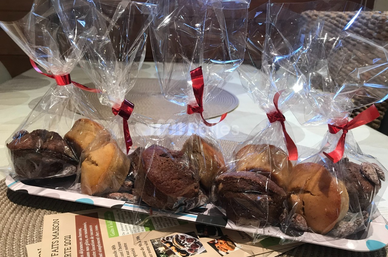Sachets transparents contenant des assortiments de muffins emballés avec des rubans rouges, posés sur une table.