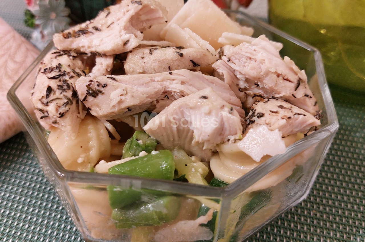 Salade composée avec pâtes, morceaux de poulet assaisonné et légumes verts, servie dans un bol en verre.