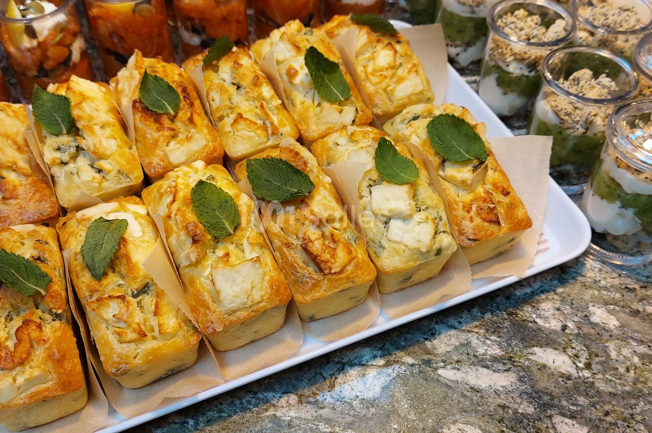 Plateau de mini cakes salés garnis de fromage et décorés de feuilles de menthe, accompagnés de verrines sucrées.