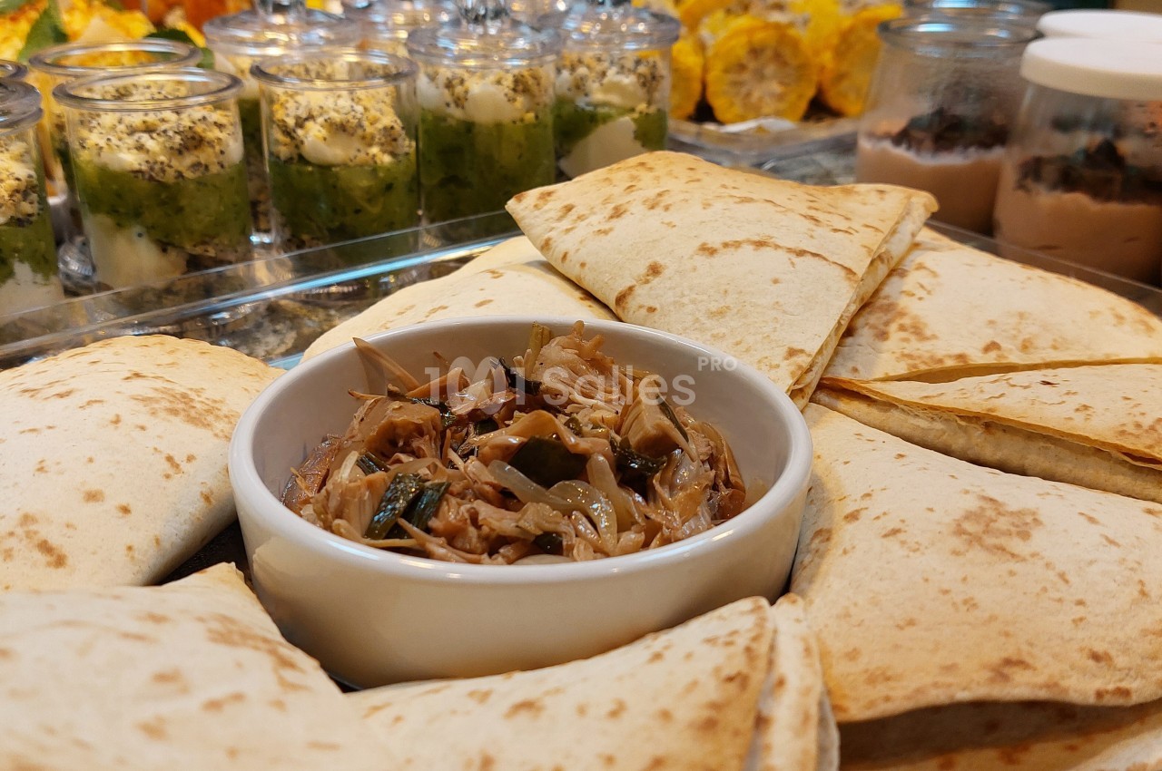 Assortiment de quesadillas entourant un bol de garniture, avec verrines et desserts en arrière-plan.