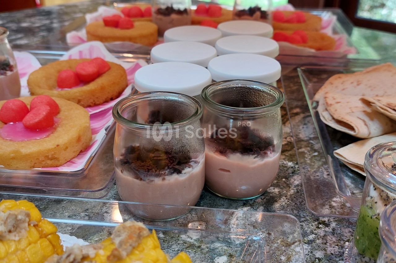 Desserts variés sur une table, incluant gâteaux, verrines au chocolat, maïs et galettes disposés sur des plateaux.