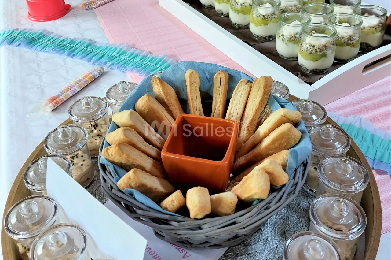 Panier de biscuits disposés en cercle autour d'un bol vide, entouré de verrines et pots en verre sur une table dressée.