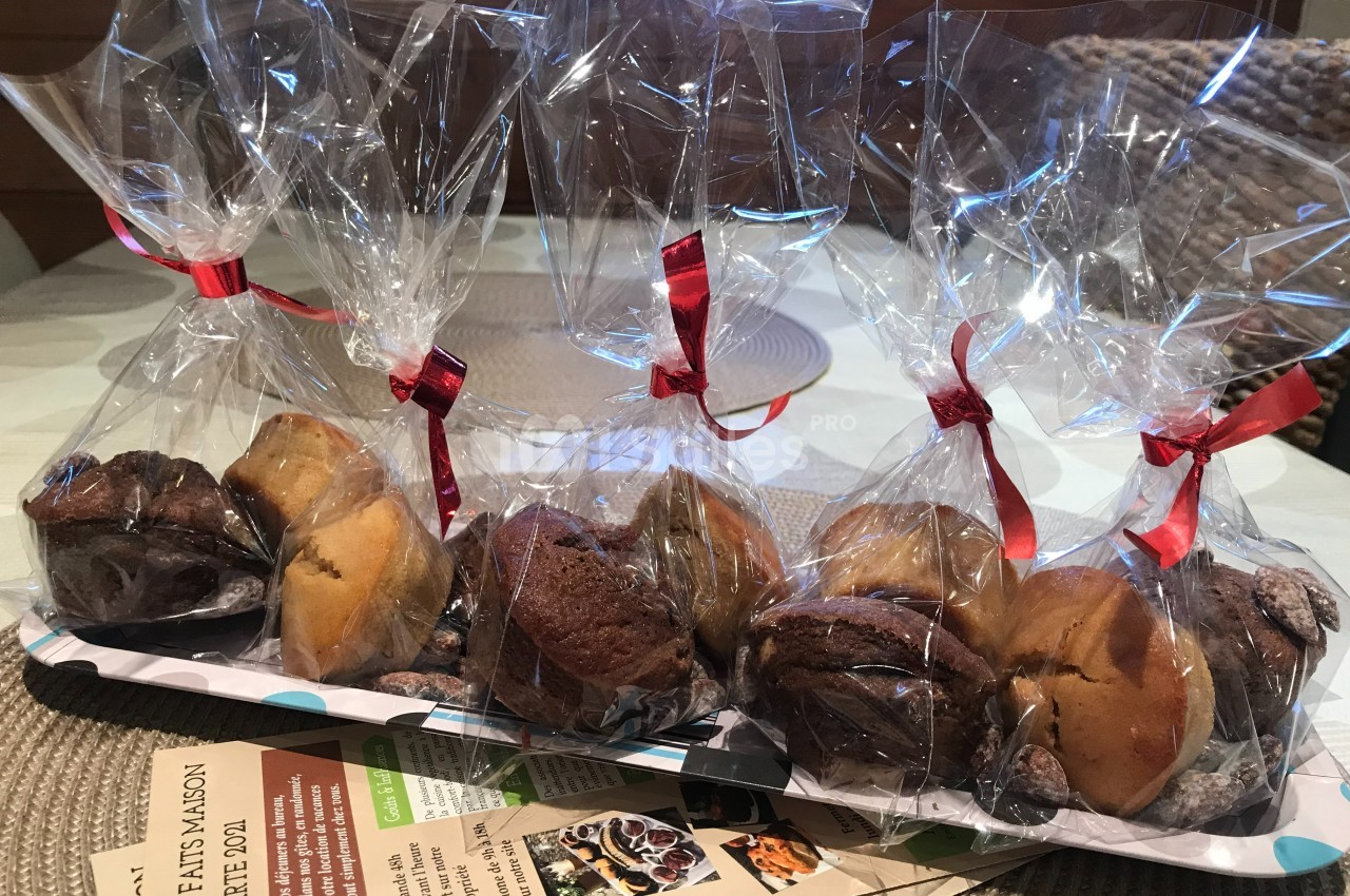 Sachets transparents contenant des assortiments de muffins emballés avec des rubans rouges, posés sur une table.