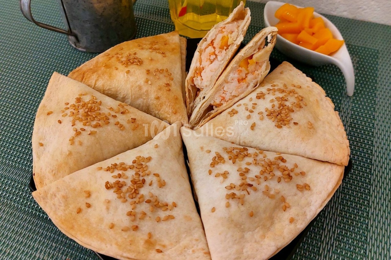 Assiette de tortillas garnies, coupées en parts, avec graines de sésame, accompagnées de morceaux de mangue.