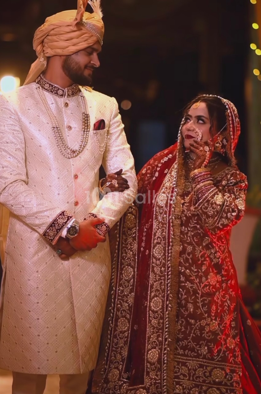 Un couple en tenue traditionnelle de mariage, l'homme en sherwani clair et la femme en sari rouge orné de broderies.