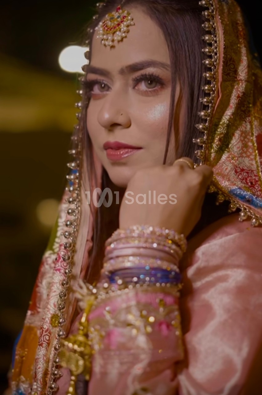 Femme portant une tenue traditionnelle ornée, avec un voile coloré et des bijoux, regardant vers l'objectif.
