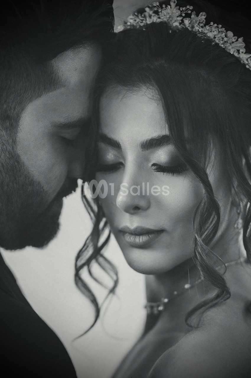 Un couple en tenue de mariage partage un moment intime, la mariée portant un diadème et des boucles élégantes.
