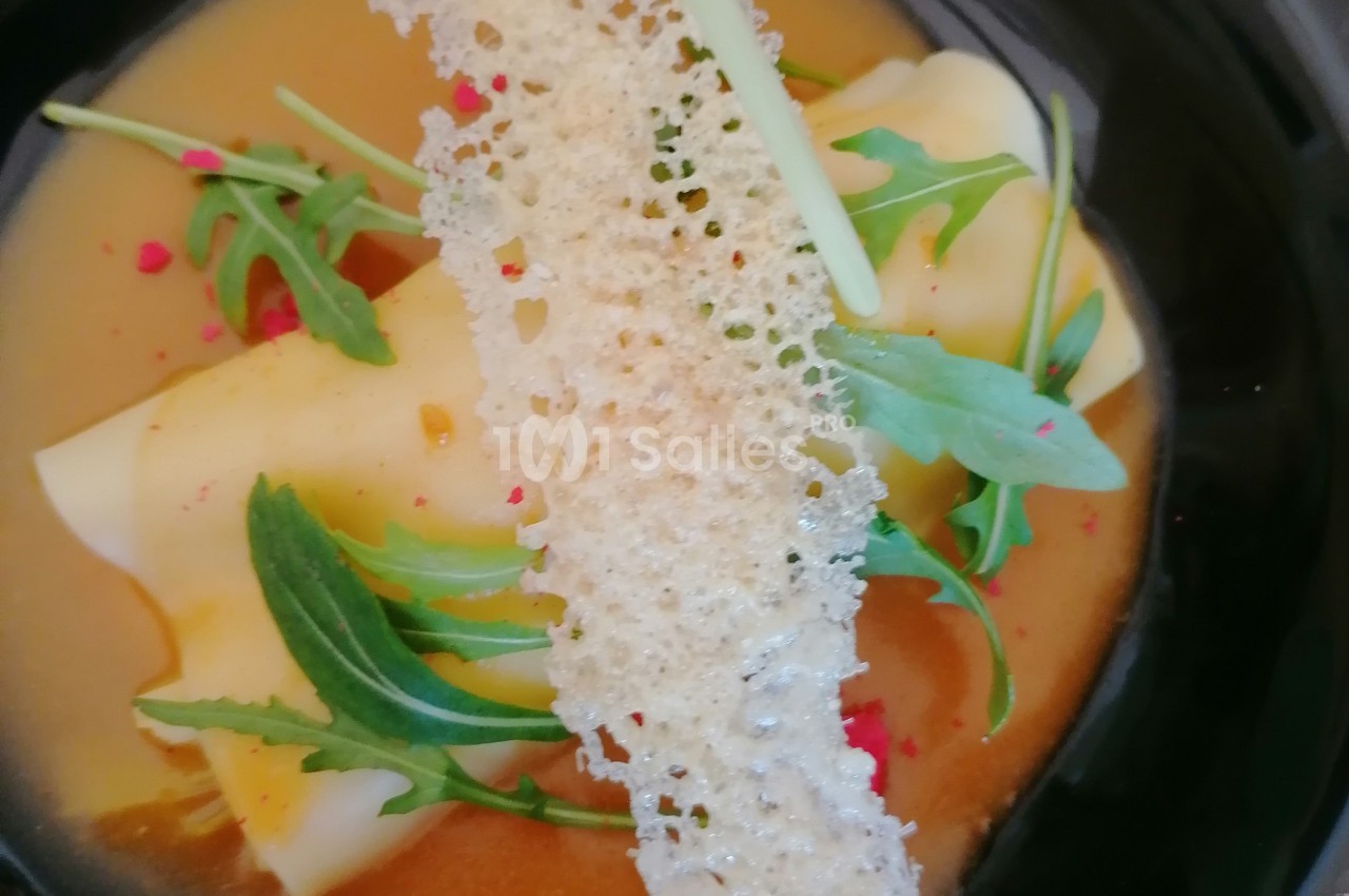 Assiette contenant des pâtes garnies, sauce orange, roquette, éclats rouges et une tuile croustillante.