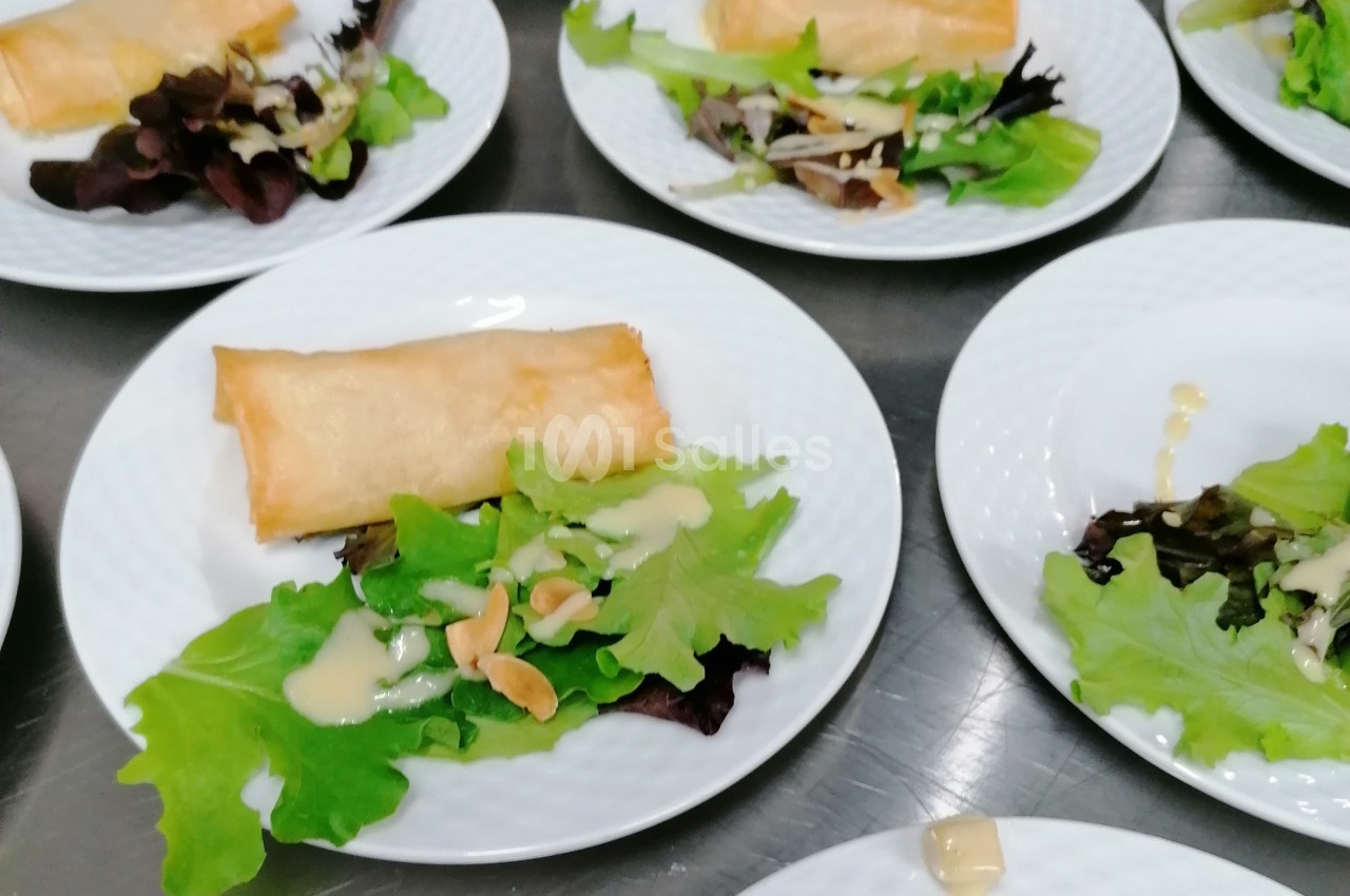 Assiette contenant une salade verte garnie de sauce et d'amandes, accompagnée d'un rouleau croustillant.