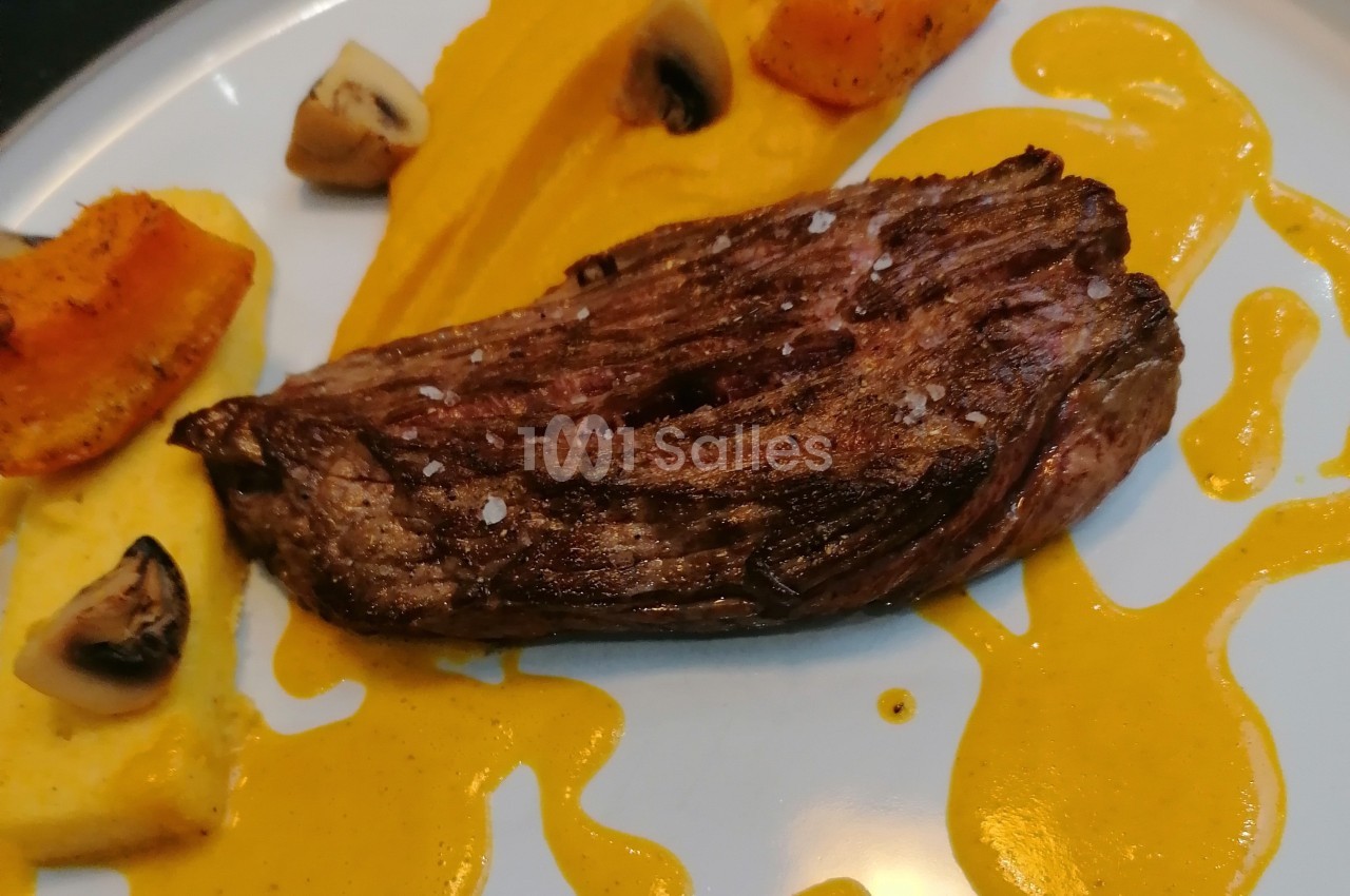Pièce de viande grillée servie avec purée orange, morceaux de polenta, champignons et sauce jaune.