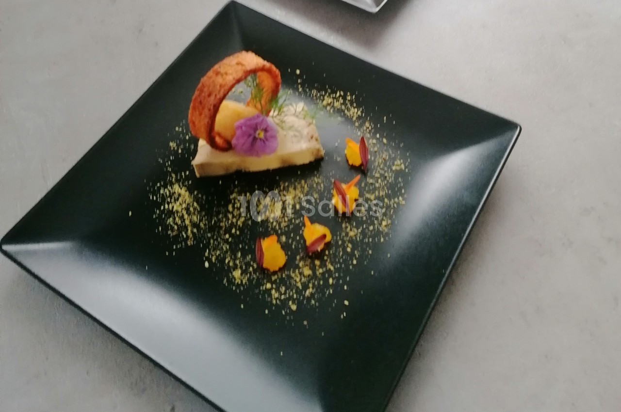 Dessert élégant sur assiette noire, décoré de fleurs comestibles, d'un biscuit courbé et de poudre colorée.