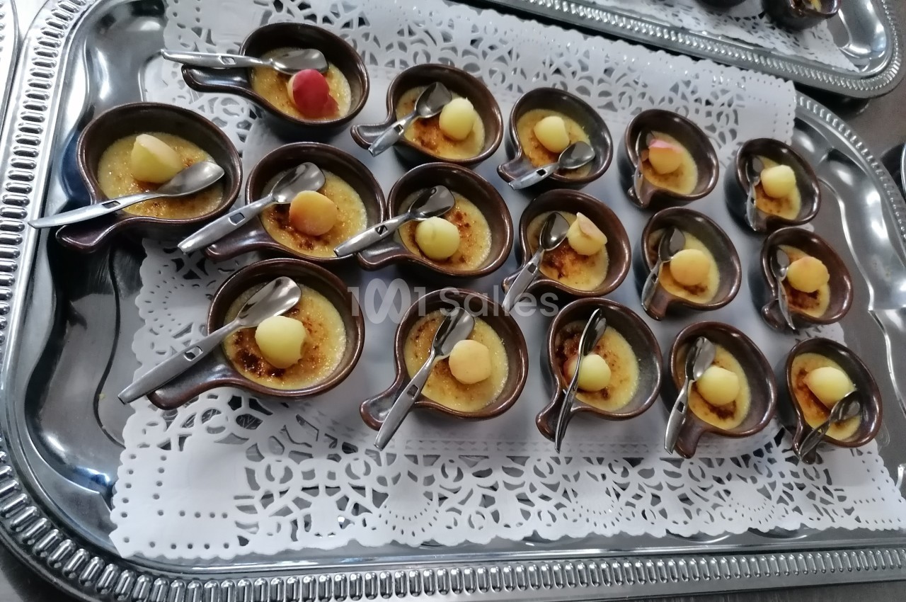 Assortiment de petites crèmes brûlées servies dans des ramequins avec cuillères sur un plateau argenté.