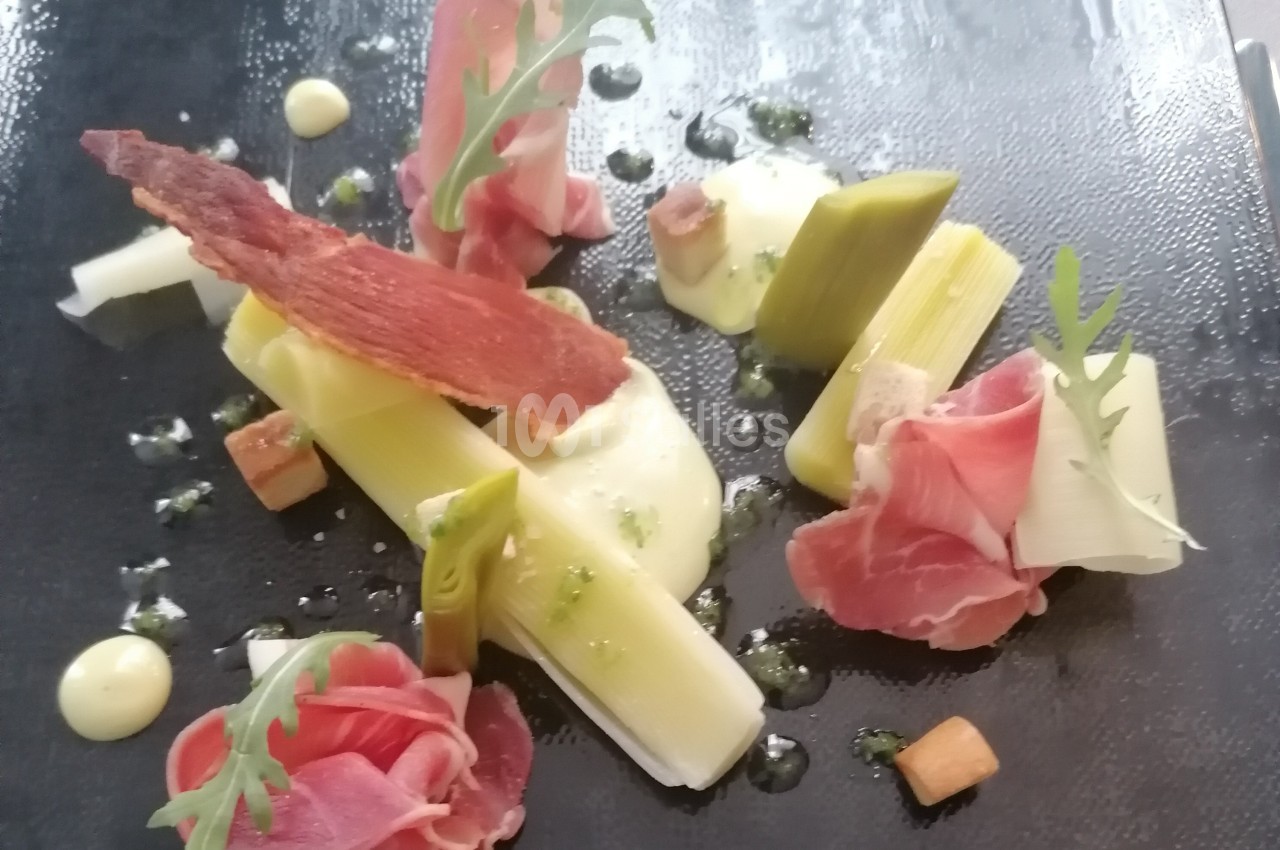 Assiette gastronomique avec poireaux, jambon cru, mousse légère, croûtons et feuilles de roquette sur ardoise noire.
