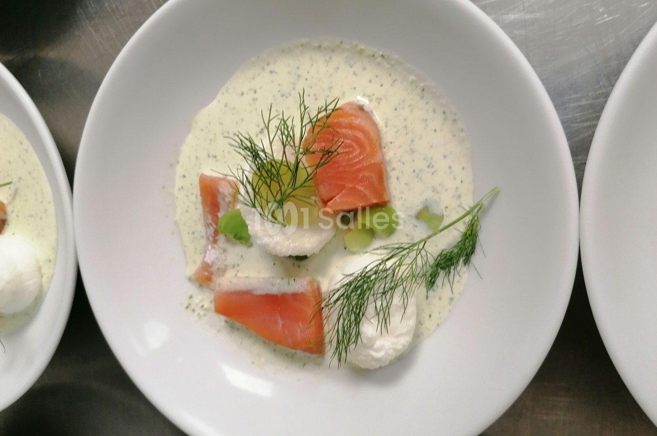 Assiette contenant du saumon fumé, crème, herbes fraîches et garnitures sur une sauce blanche.