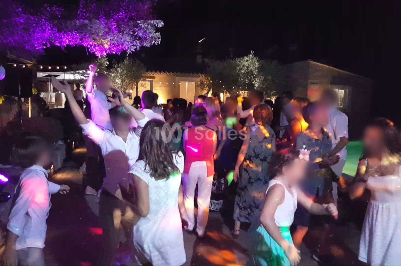 Groupe de personnes dansant lors d'une fête en soirée, éclairée par des lumières colorées.