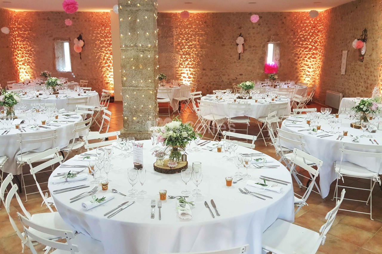 Salle de réception décorée avec des tables rondes dressées, nappes blanches et arrangements floraux.