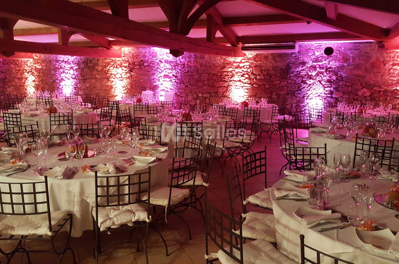 Salle de réception décorée avec des tables rondes dressées, éclairage rose et murs en pierre apparente.
