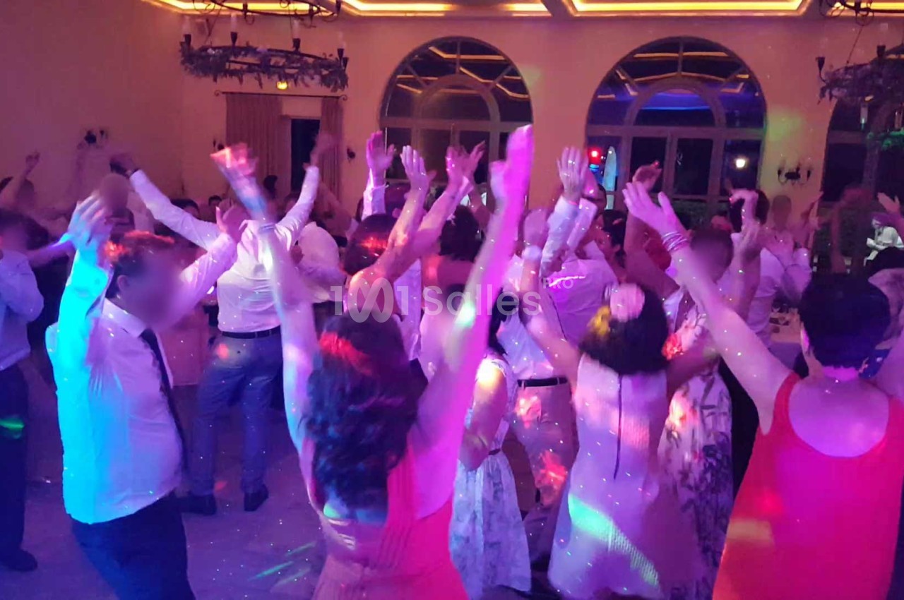 Groupe de personnes dansant sous des lumières colorées dans une salle avec de grandes fenêtres et un plafond éclairé.
