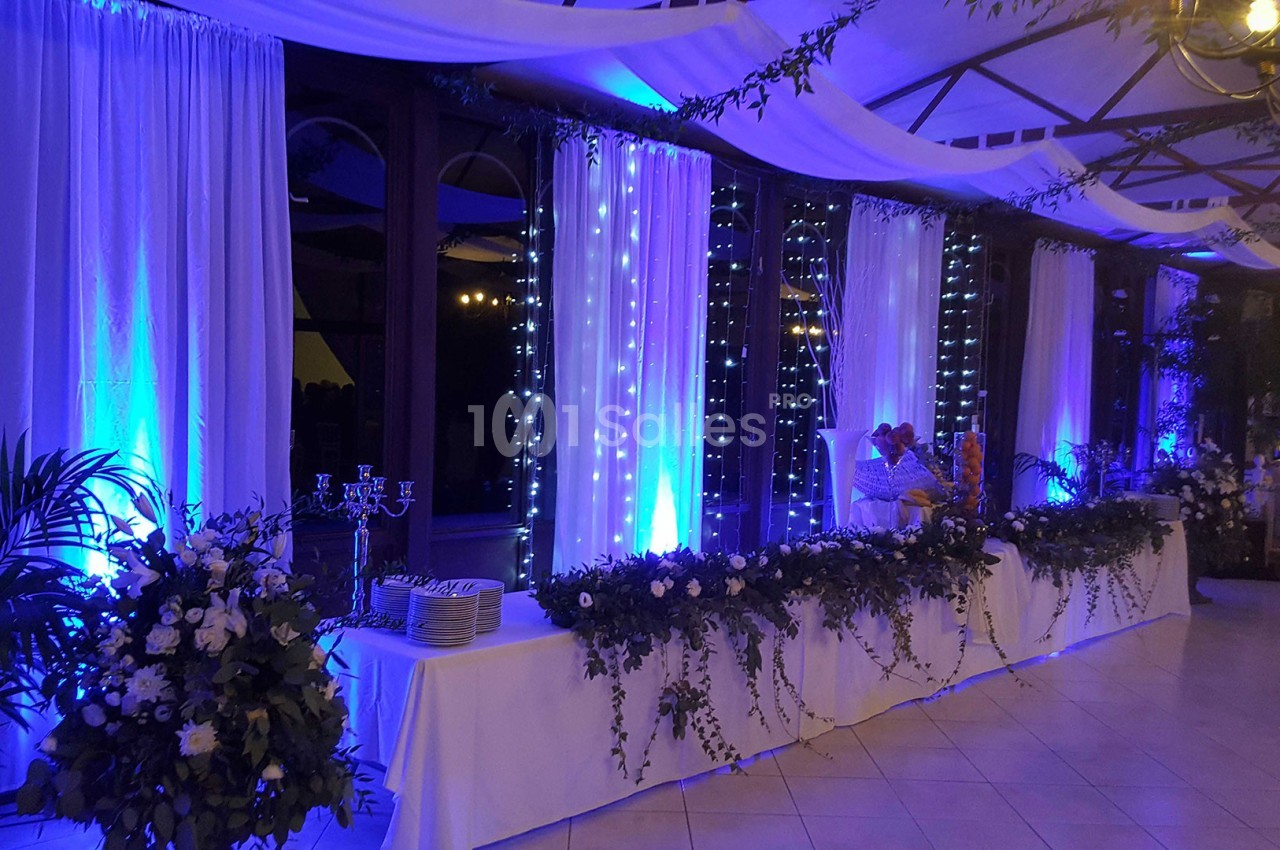 Salle de réception décorée avec des guirlandes lumineuses, des rideaux blancs et des arrangements floraux.
