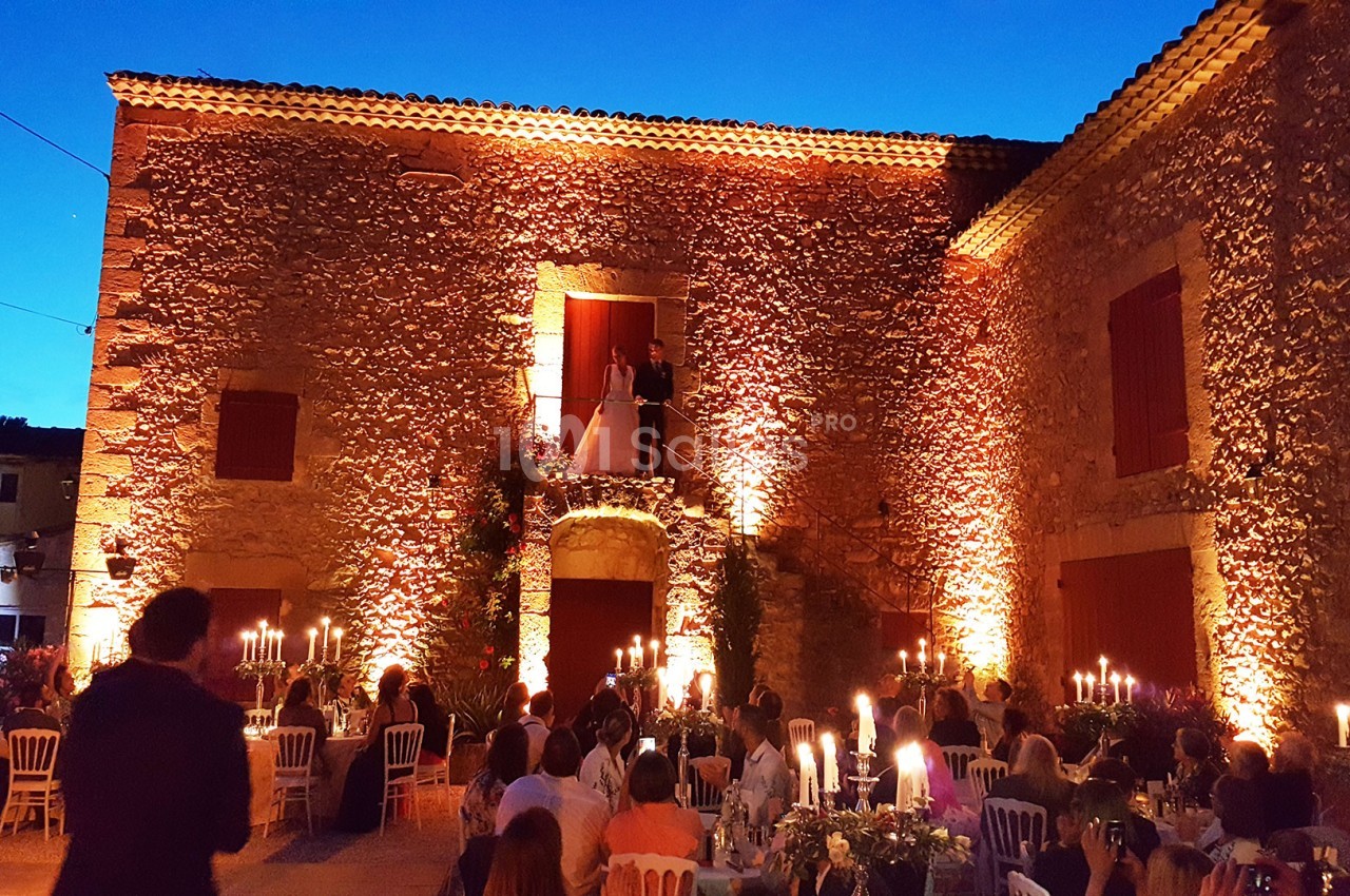 Façade en pierre éclairée lors d'une réception en soirée, avec des invités assis autour de tables illuminées.