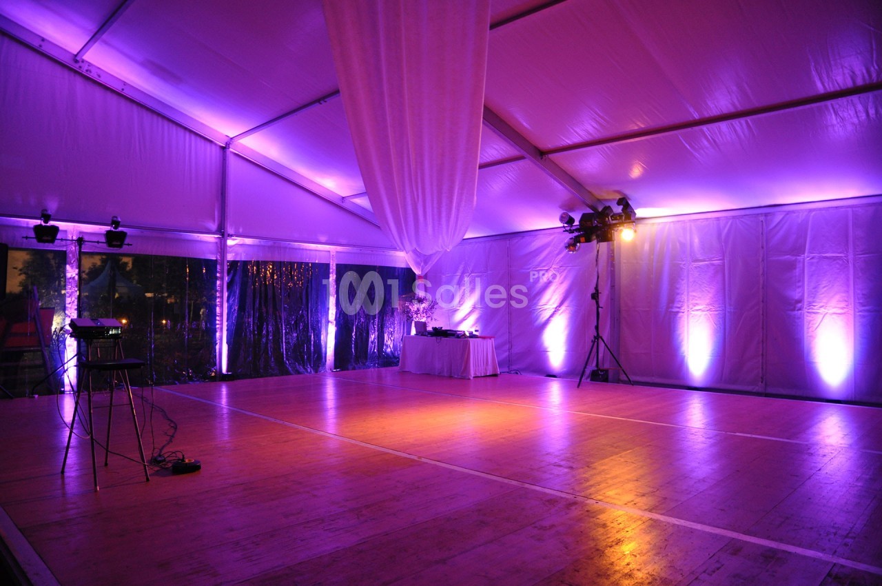 Intérieur d'une tente événementielle éclairée par des lumières violettes, avec une piste de danse en bois.
