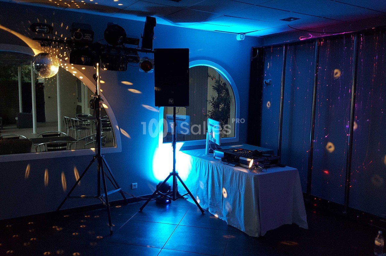 Salle de réception avec éclairage coloré, table de mixage pour DJ et jeux de lumière projetés sur les murs.