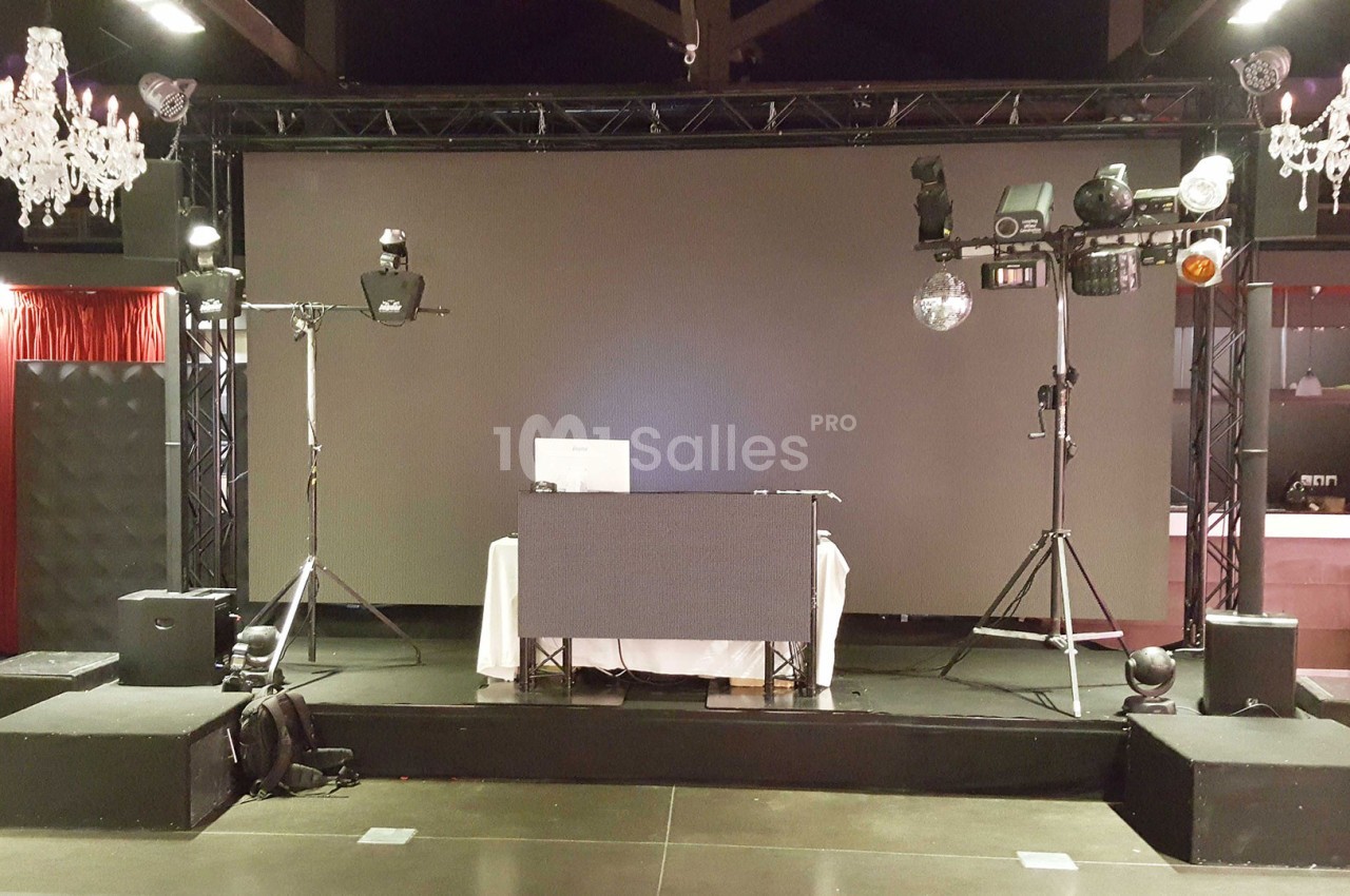 Scène avec équipement de sonorisation et éclairage, incluant une table de DJ devant un écran blanc.