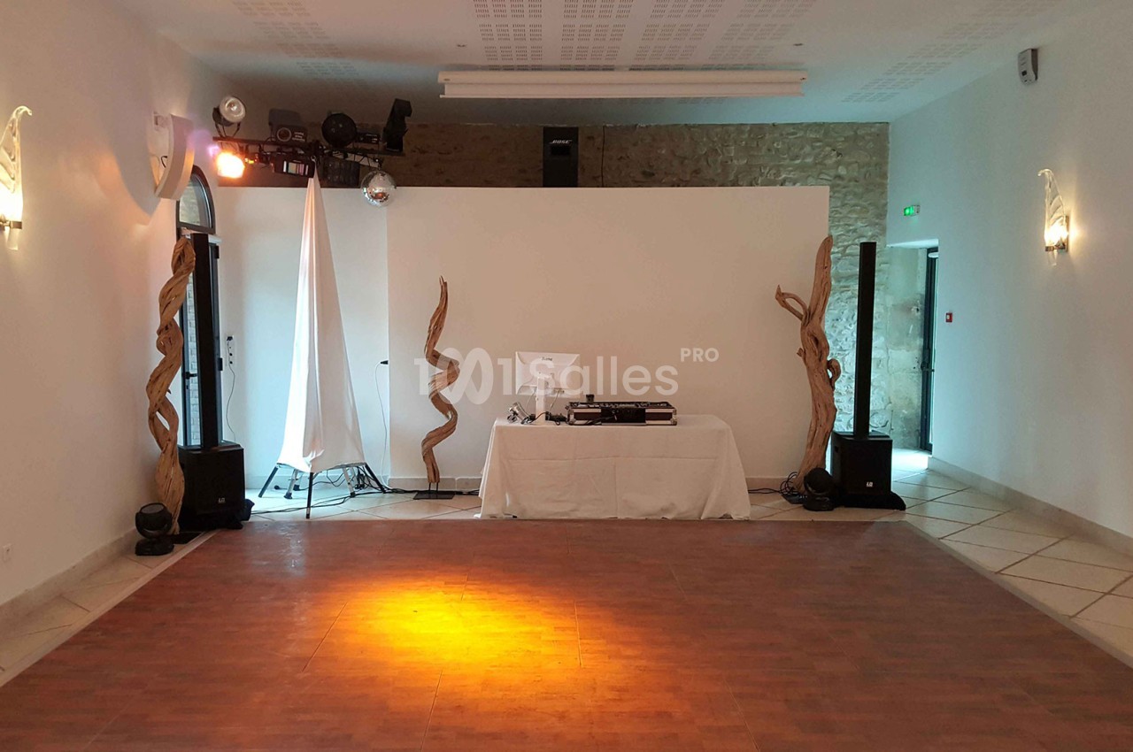 Salle vide avec parquet, éclairage tamisé, table de DJ équipée et décorations en bois torsadé.