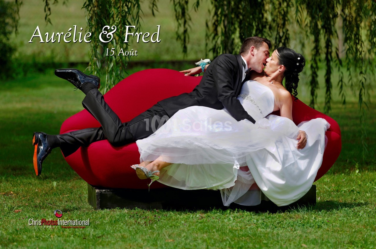 Un couple en tenue de mariage s'embrasse allongé sur un canapé rouge dans un jardin verdoyant.