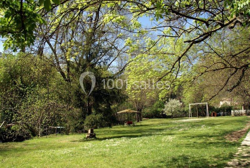 Grand jardin verdoyant avec arbres, pelouse, balançoire et parasol sous un ciel bleu clair.
