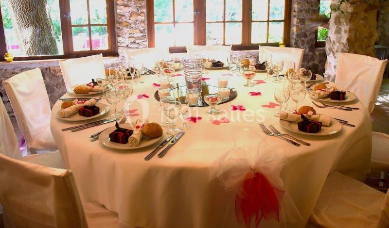 Table ronde élégamment dressée avec nappes blanches, couverts, cadeaux, pétales roses et lumière naturelle.