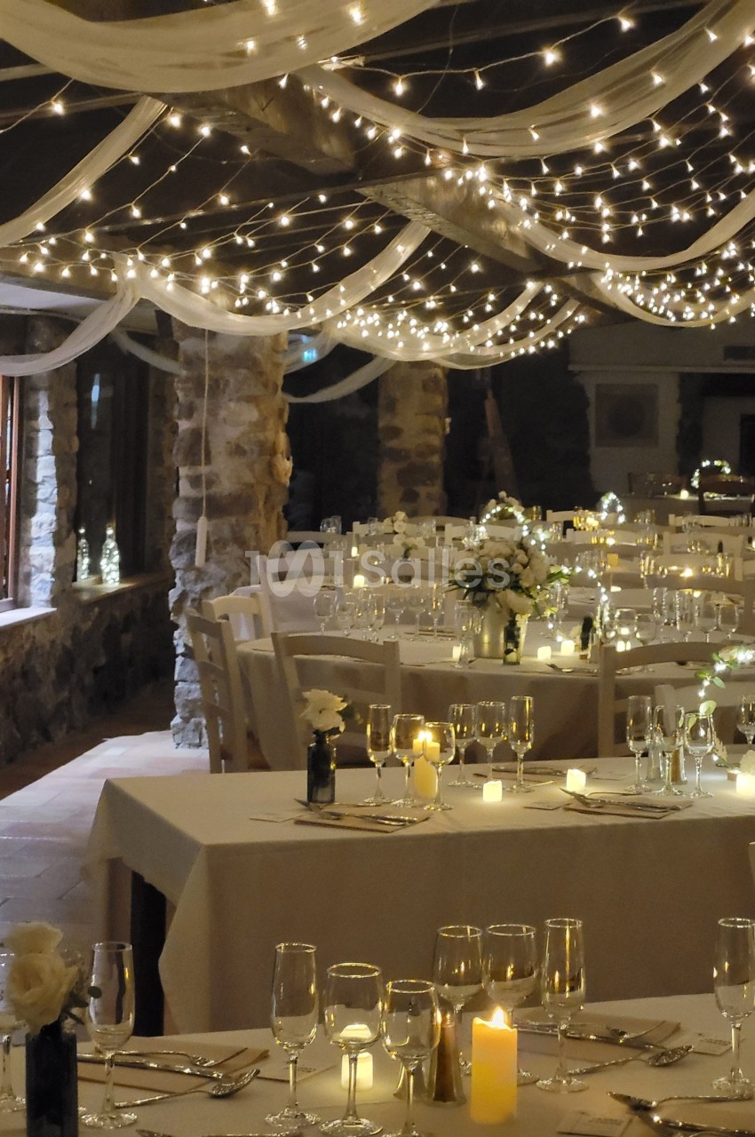 Salle de réception décorée avec des guirlandes lumineuses, des tables dressées et des centres de table fleuris.