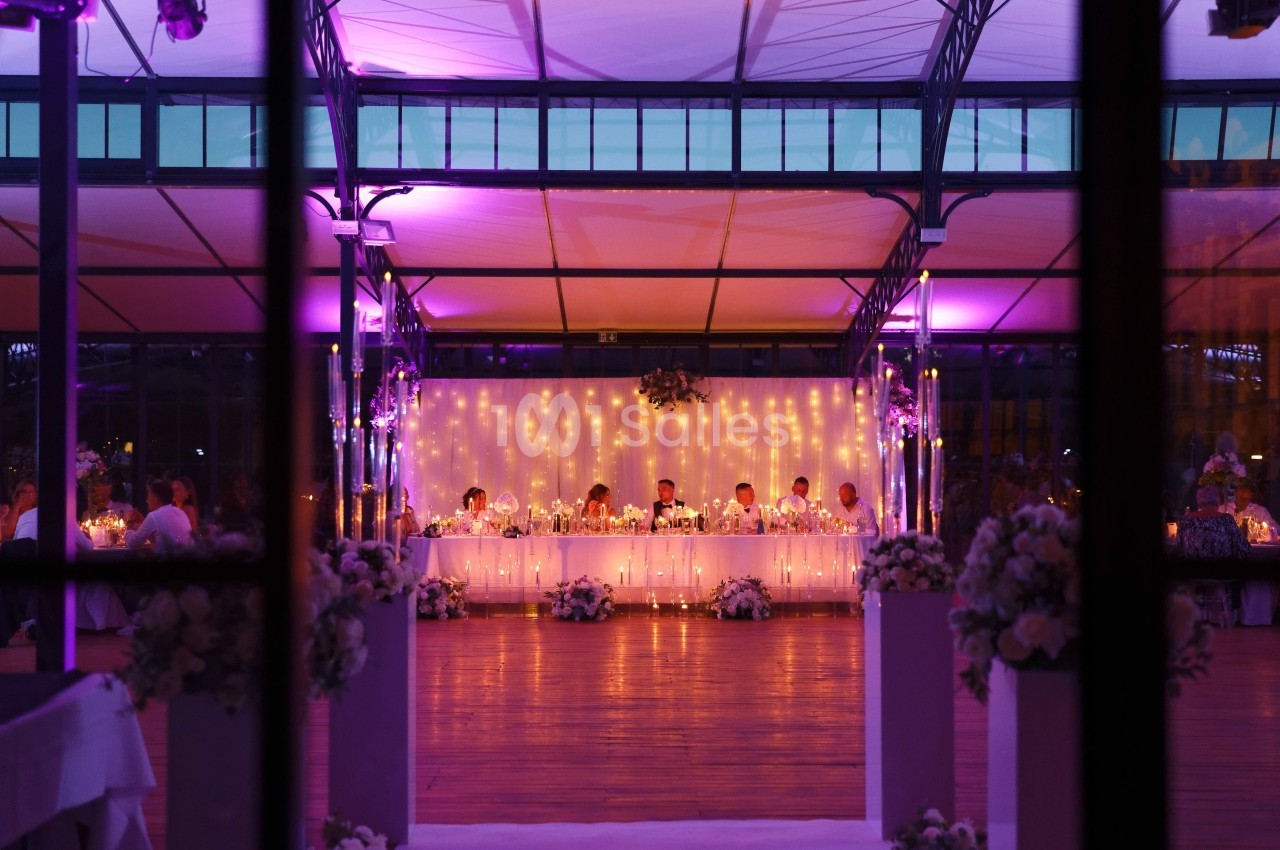Salle de réception décorée avec des lumières tamisées et une longue table festive entourée de fleurs.