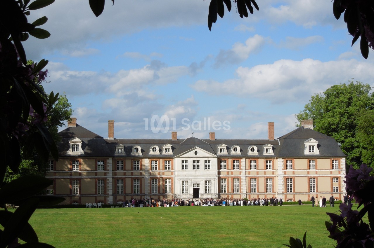 Façade d'un château en briques et pierre entouré de verdure, avec des visiteurs rassemblés sur la pelouse.