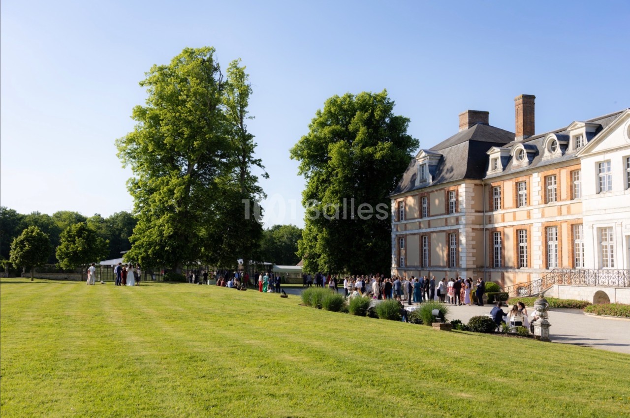 Groupe de personnes rassemblées devant un château entouré de pelouses et d'arbres par une journée ensoleillée.