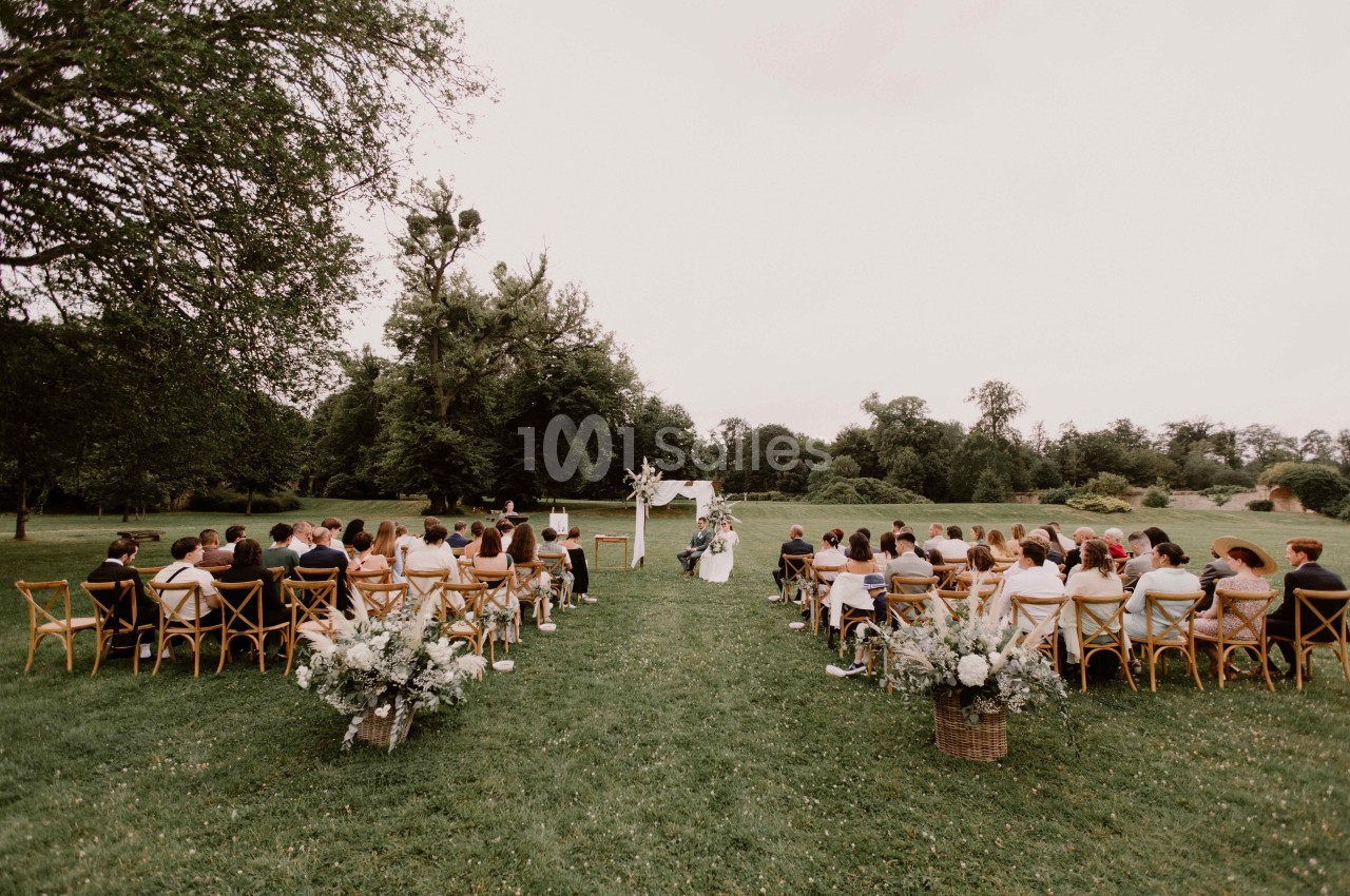 Cérémonie de mariage en plein air avec invités assis sur des chaises en bois, entourés de verdure et de décorations florales.
