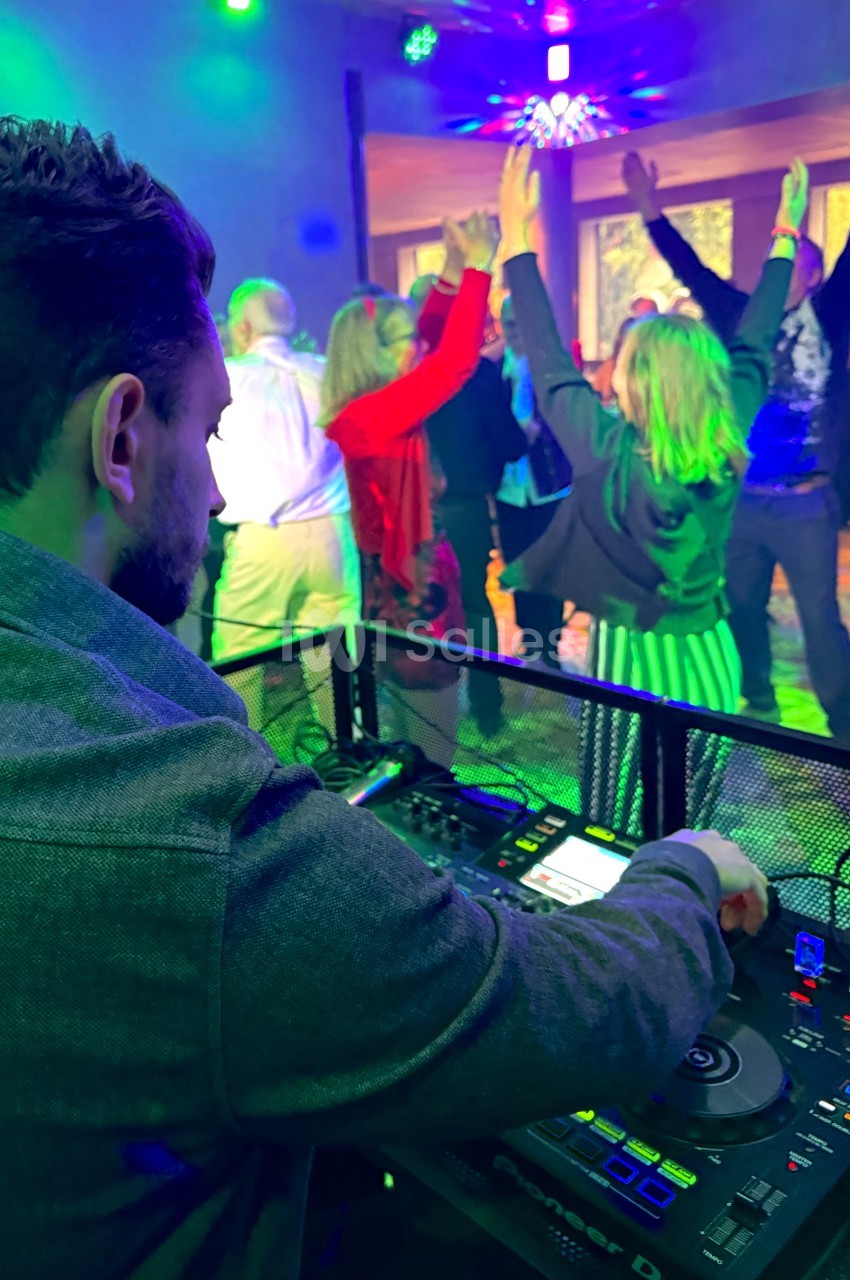 Un DJ mixe de la musique tandis que des personnes dansent sous des lumières colorées dans une salle festive.