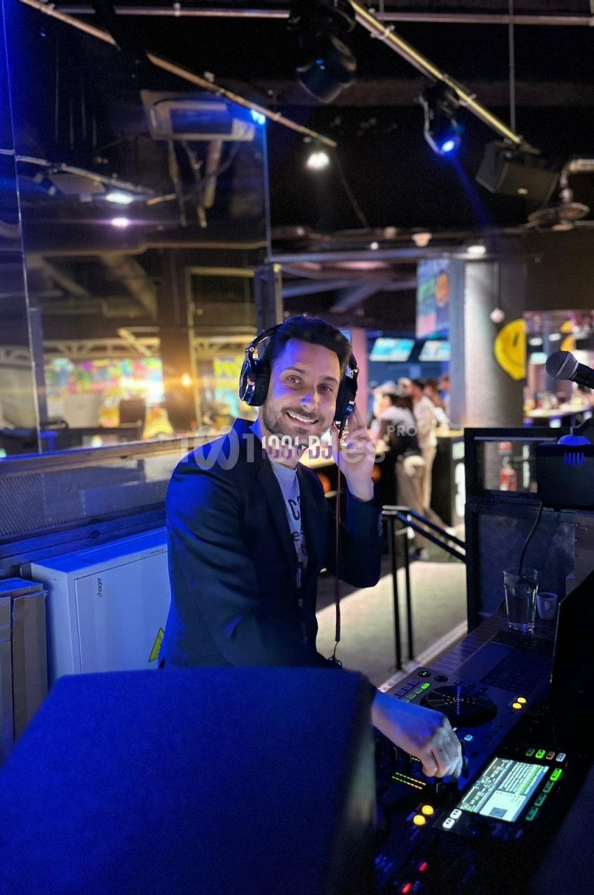 Un DJ souriant mixe de la musique dans un espace intérieur éclairé par des lumières colorées.