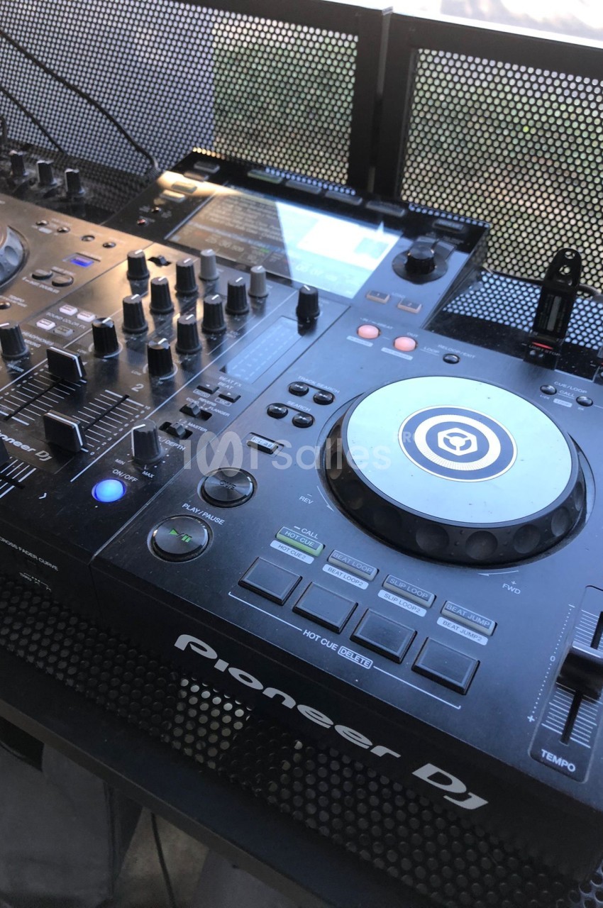 Table de mixage DJ avec platine, boutons et commandes, posée sur une surface perforée en extérieur.