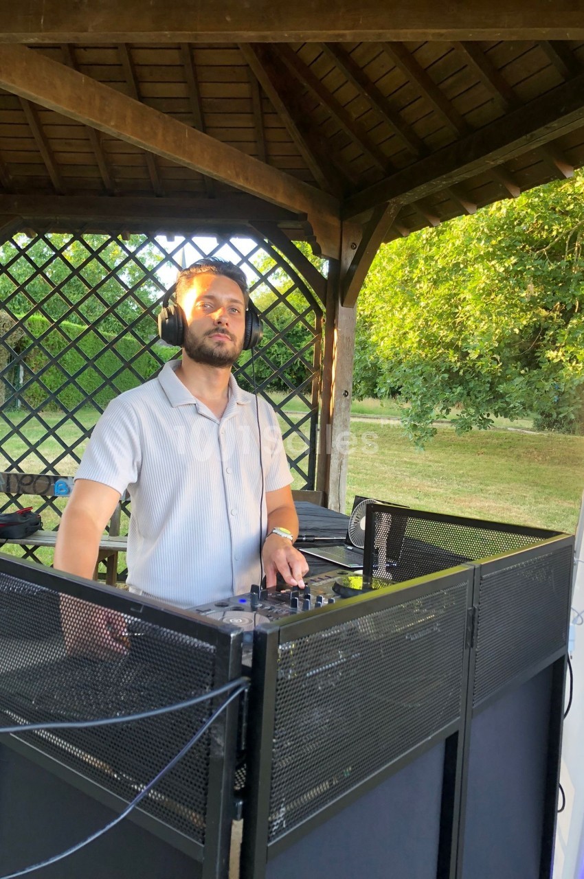 Un DJ mixant de la musique en extérieur sous un kiosque en bois, entouré de verdure.