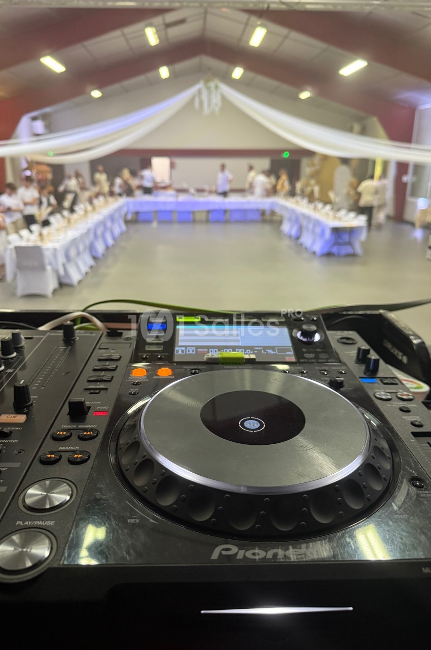 Vue depuis une table de mixage dans une salle de réception, avec des tables dressées et des invités en arrière-plan.