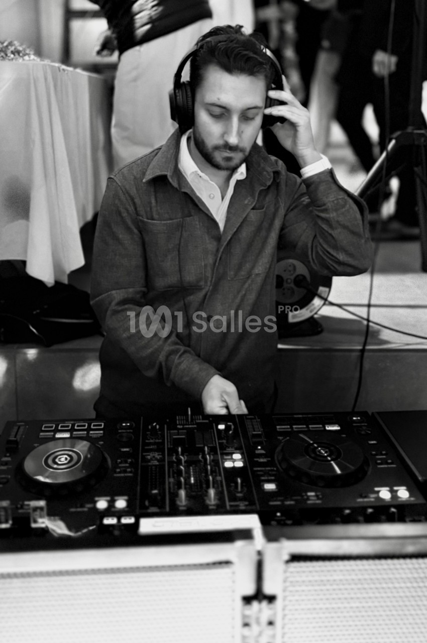 Un DJ mixant de la musique sur une table de mixage, portant un casque audio dans un environnement intérieur.
